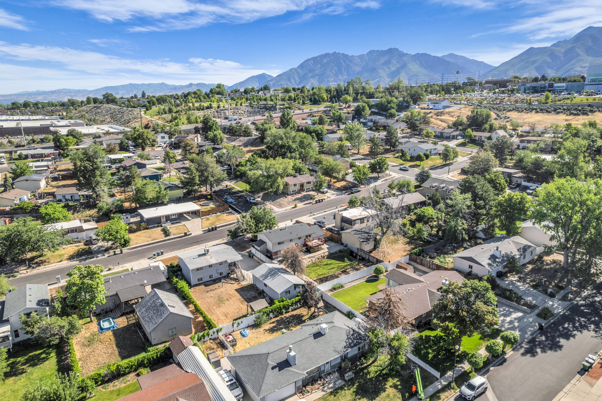 Expansive neighborhood setting featuring a range of single-family residences, mature trees, paved streets, and mountainous surroundings