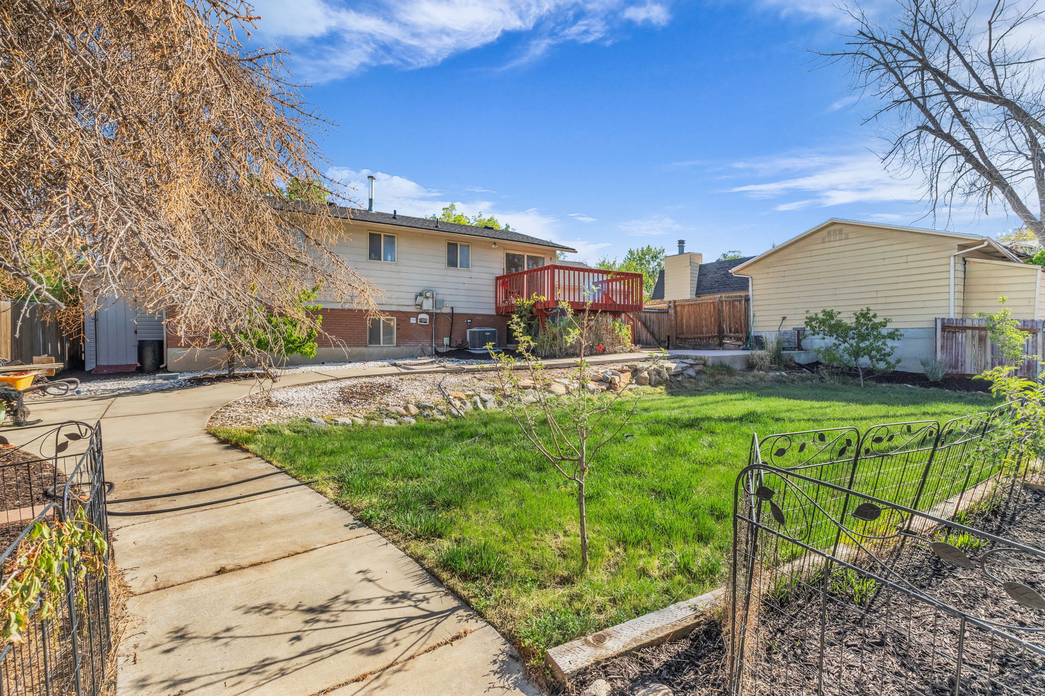 Landscaped backyard featuring a red wood deck, a manicured lawn, a concrete pathway, a detached shed, and wood fencing