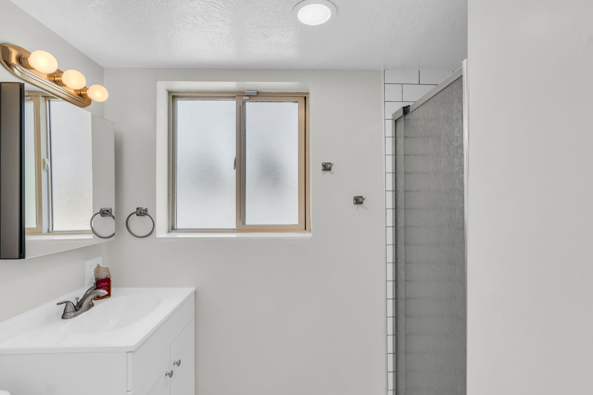 Bathroom featuring a single vanity with built-in storage, a medicine cabinet, an opaque window, a shower with a sliding door, and a recessed ceiling light