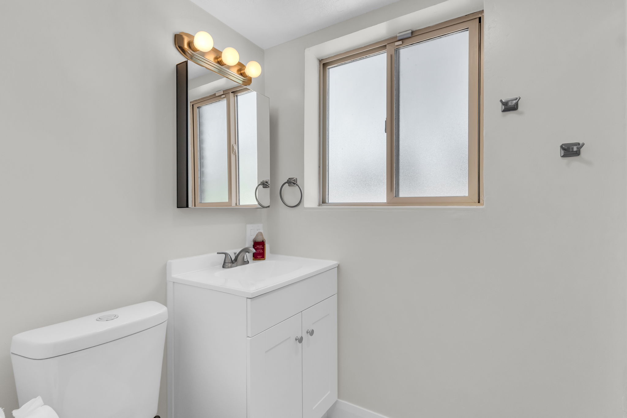 Bathroom featuring a white vanity with integrated sink, chrome faucet, and a wall-mounted medicine cabinet with integrated lighting