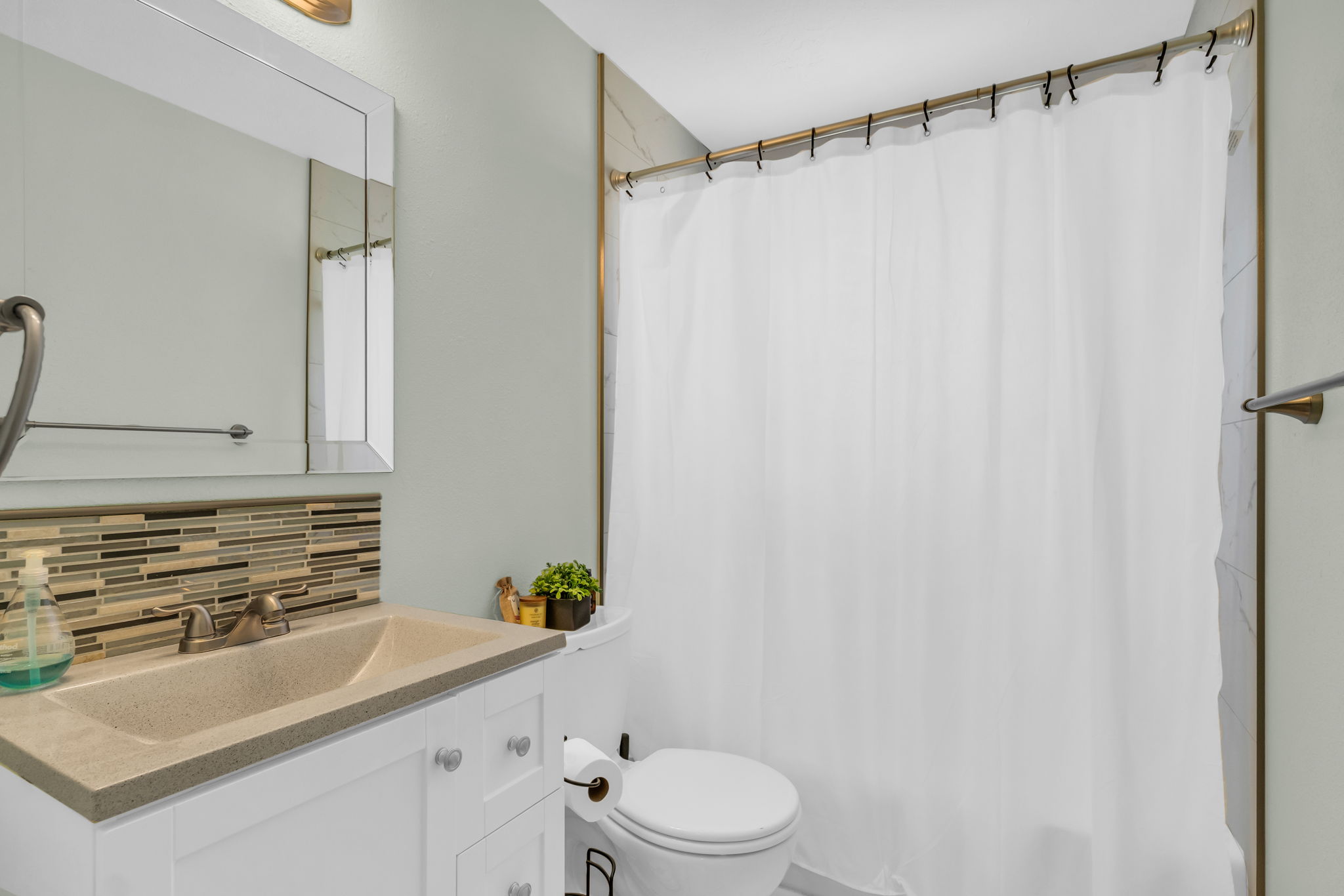 Bathroom featuring a white vanity with brushed nickel hardware, integrated sink, and a mosaic tile backsplash