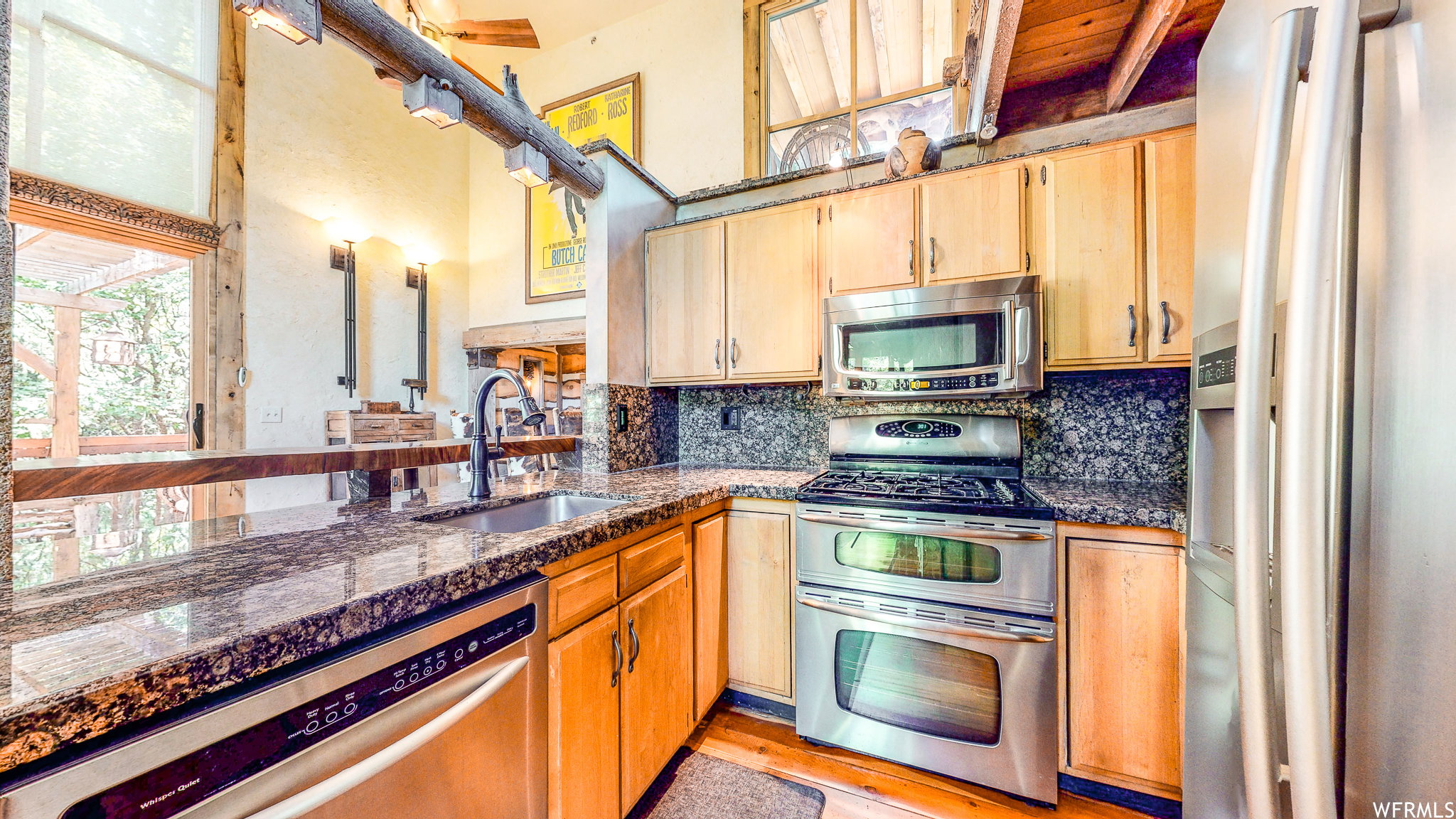Kitchen featuring stainless steel appliances, granite countertops, natural wood cabinetry, a built-in dishwasher, and an integrated double oven range with an overhead microwave