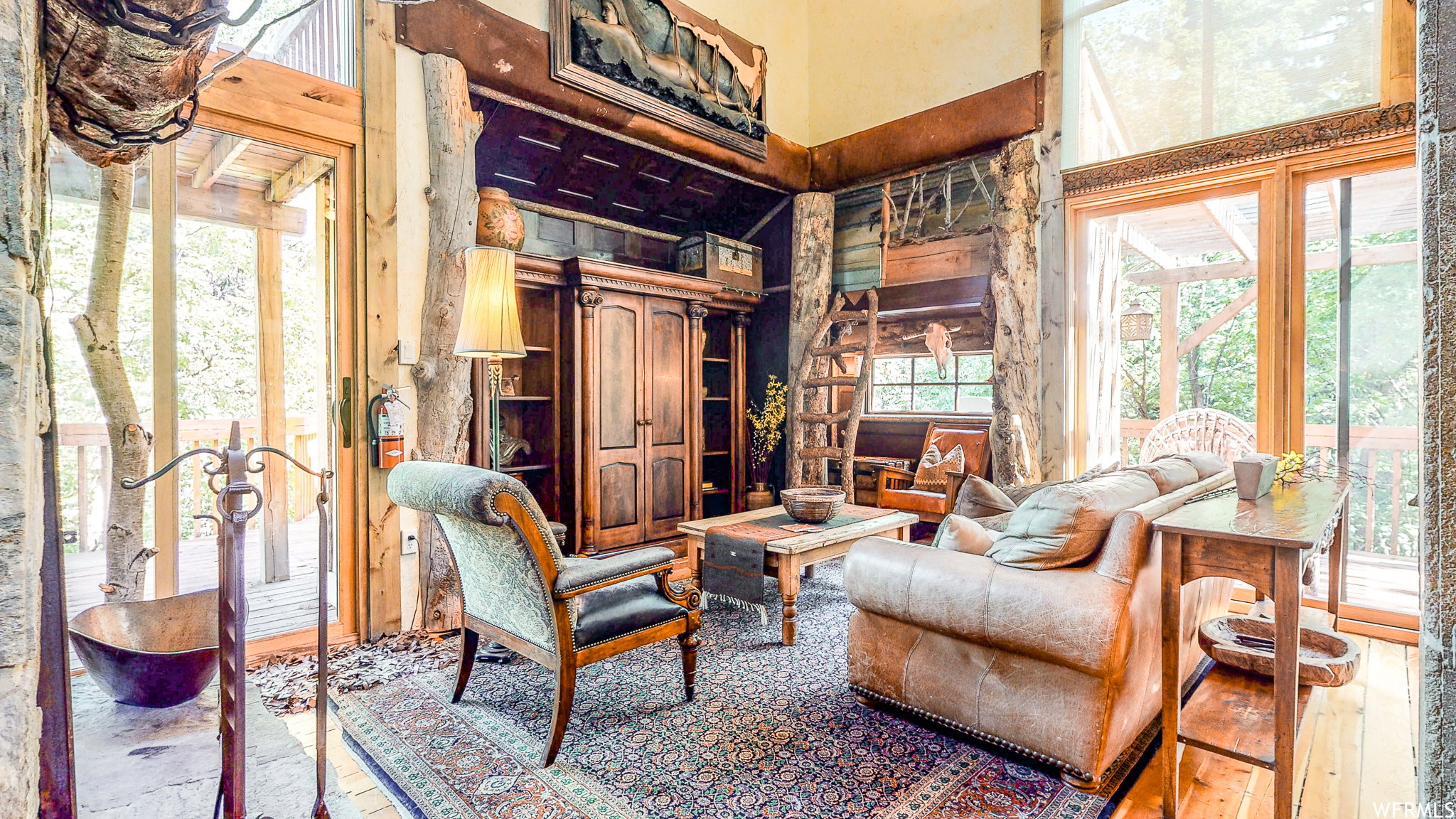 Vaulted living room featuring wood-finish flooring, exposed natural wood structural elements, custom built-in cabinetry, and expansive glass sliding doors opening to an outdoor deck