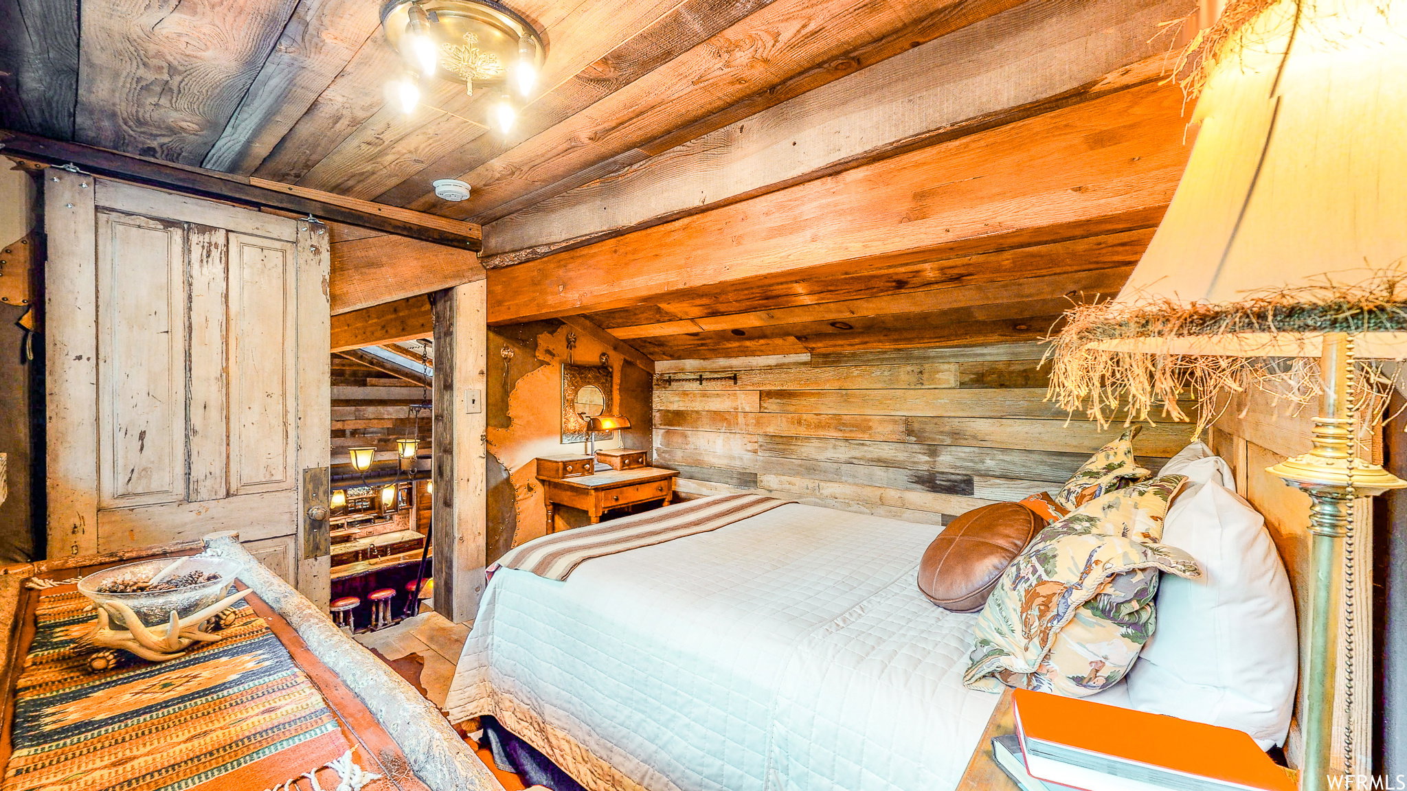 Attic bedroom featuring exposed wood beam ceiling, wood-paneled walls, barn door access, and a built-in wooden nightstand