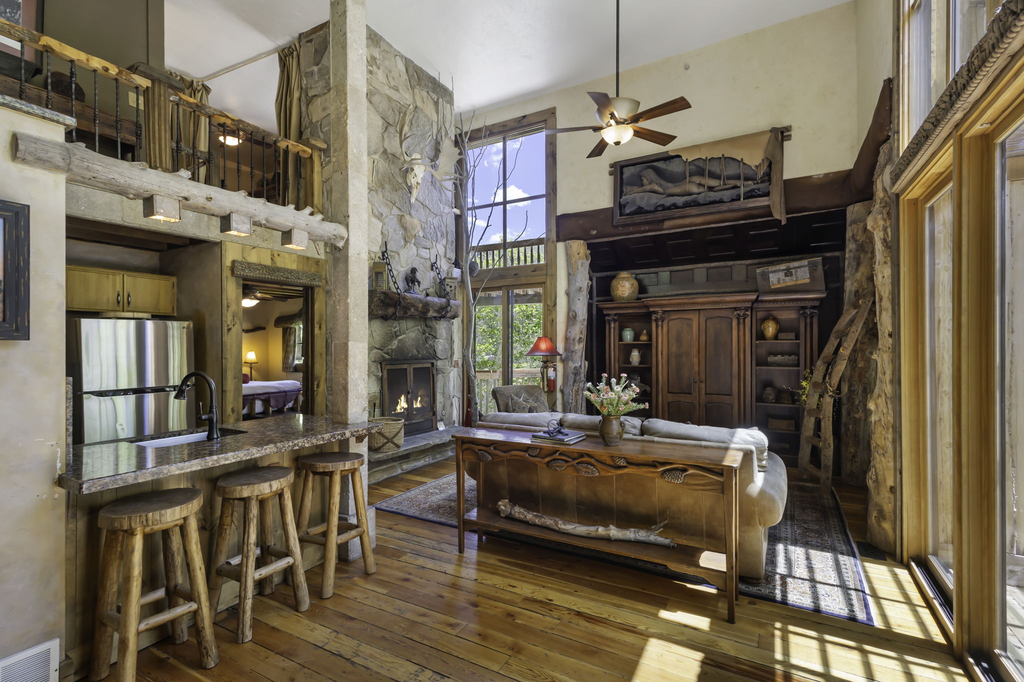 Spacious living area featuring a stone fireplace, high ceilings, large windows, wood-finish flooring, and a built-in media center