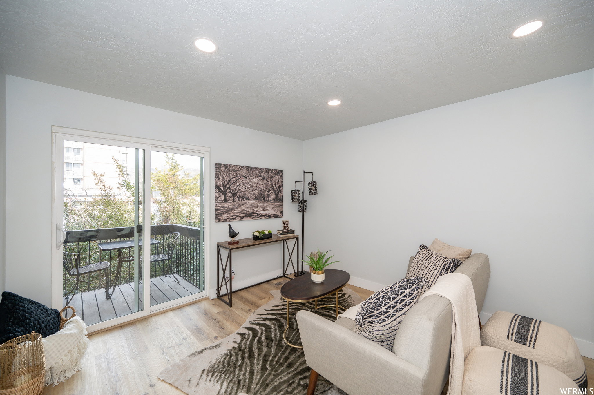 Living area featuring light wood-finish flooring, recessed lighting, and a glass sliding door opening to a private balcony