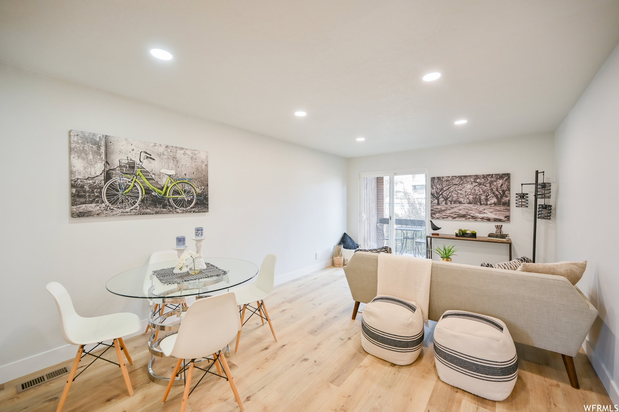 Open-concept living space with light wood-finish flooring, recessed lighting, and a sliding glass door leading to an exterior balcony
