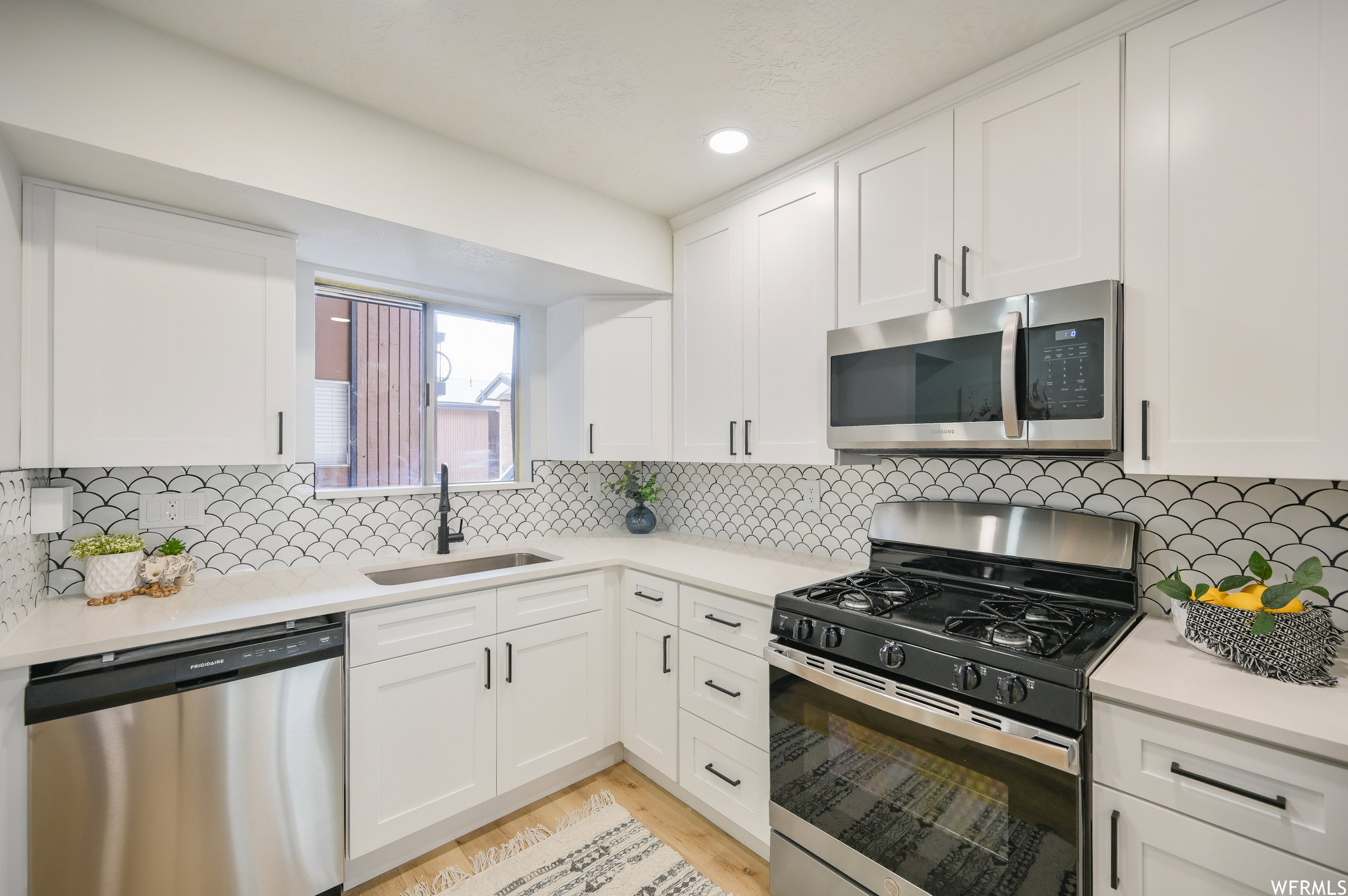 Modern kitchen featuring white shaker cabinetry, stainless steel appliances, and a unique scallop-patterned backsplash