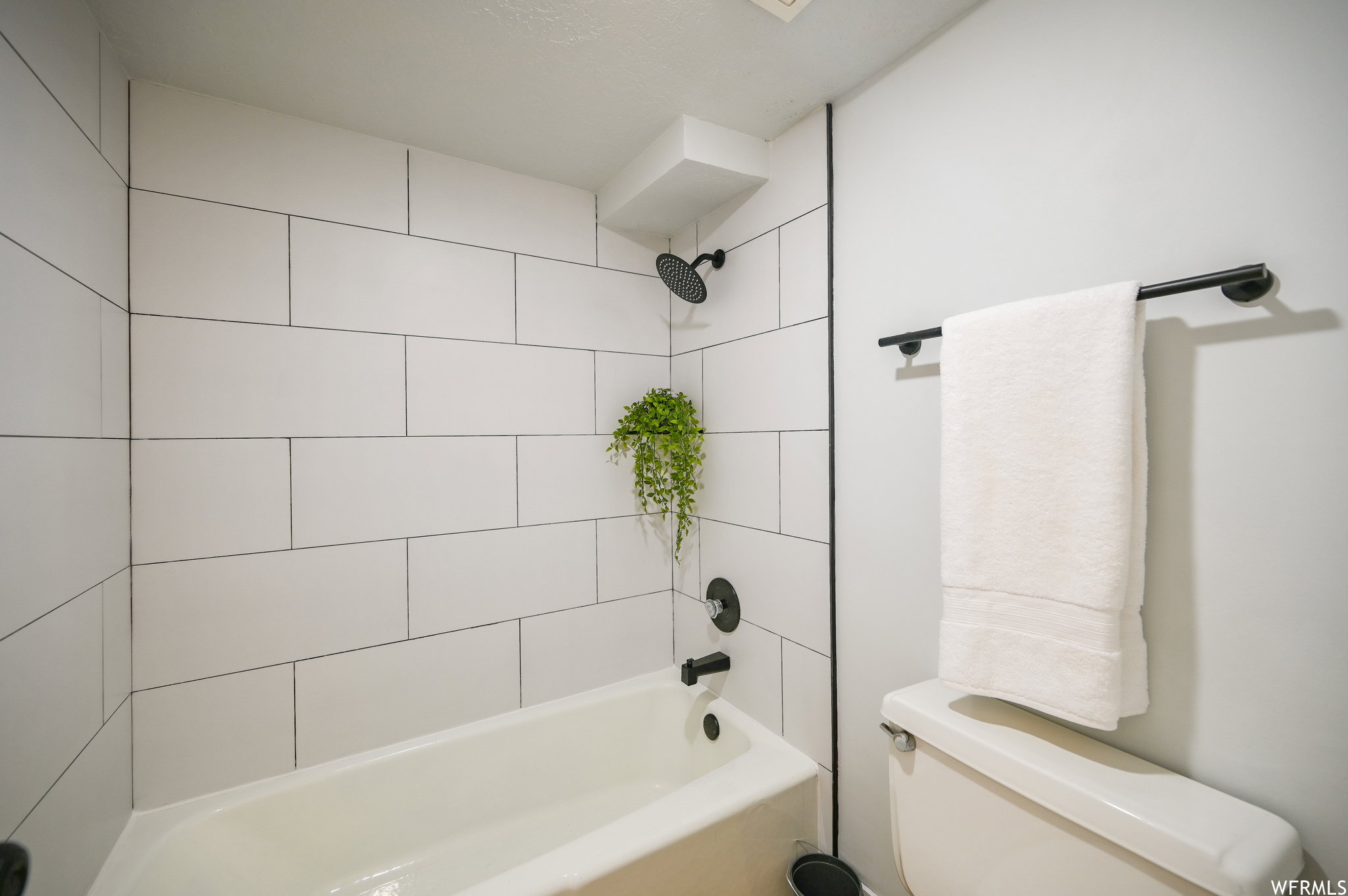 Bathroom tub and shower combination featuring white subway tile surround, matte black shower fixtures, and a white porcelain tub