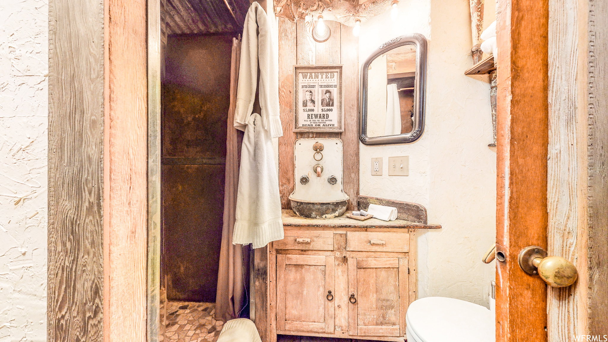 Bathroom featuring a rustic wood vanity with integrated basin, framed wall mirror, and an adjacent shower enclosure with a dark curtain