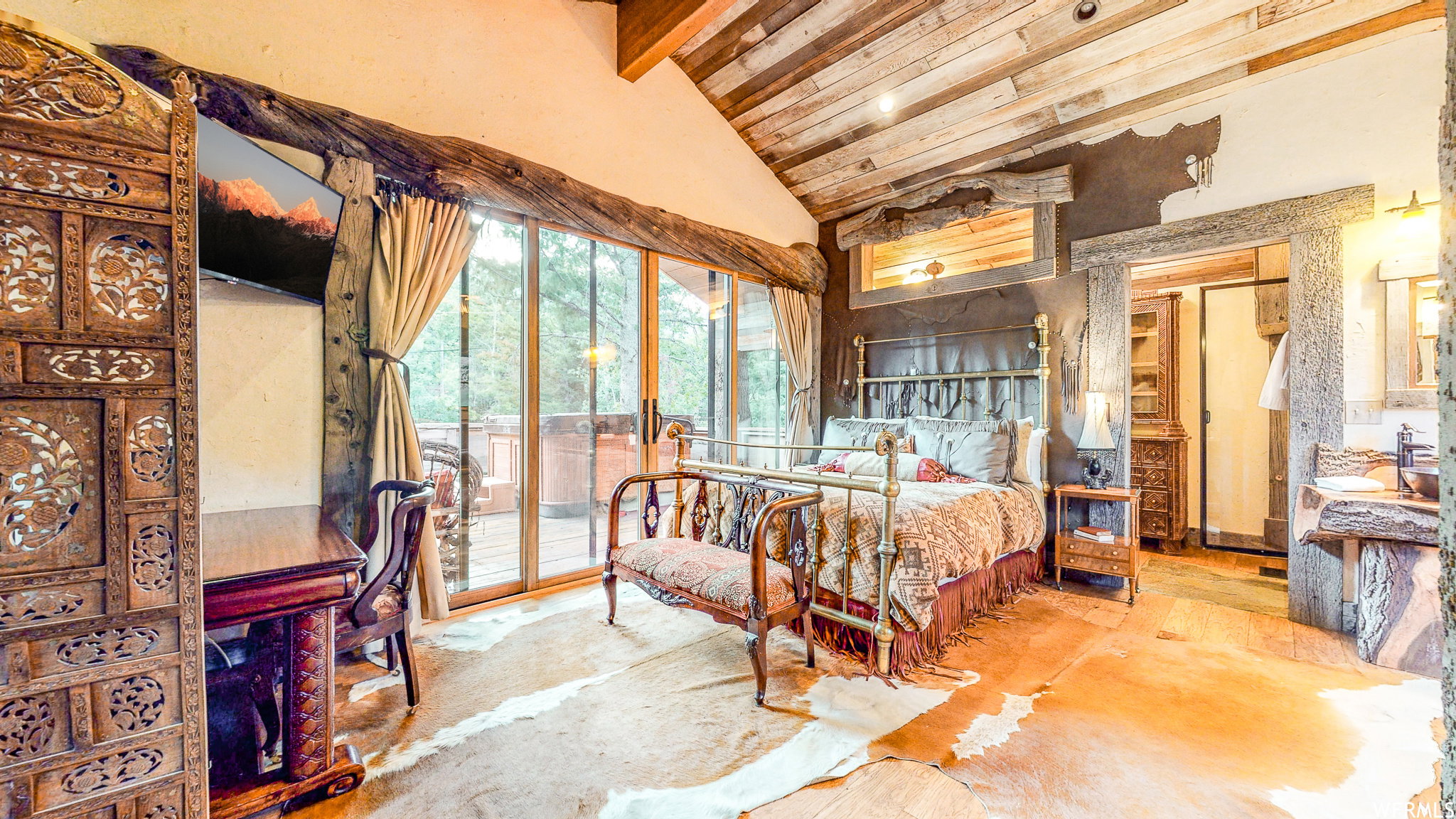 Vaulted wood plank ceiling over a bedroom featuring sliding glass doors, a brass bed frame, and a carved wood screen