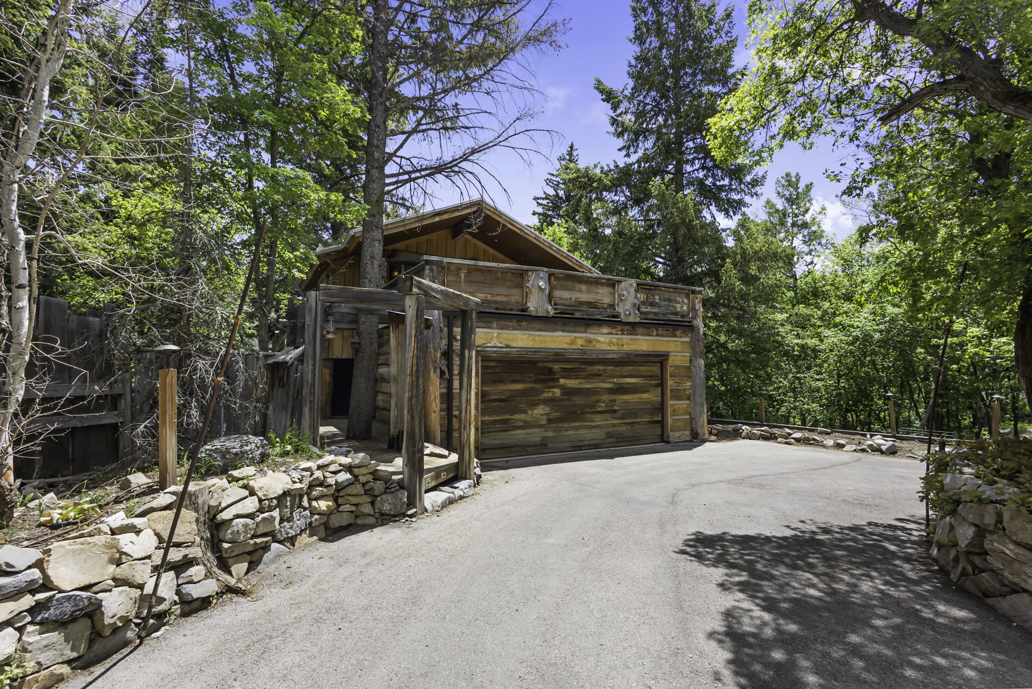 Integrated garage with wood-finish door, extensive paved driveway, and stone retaining walls
