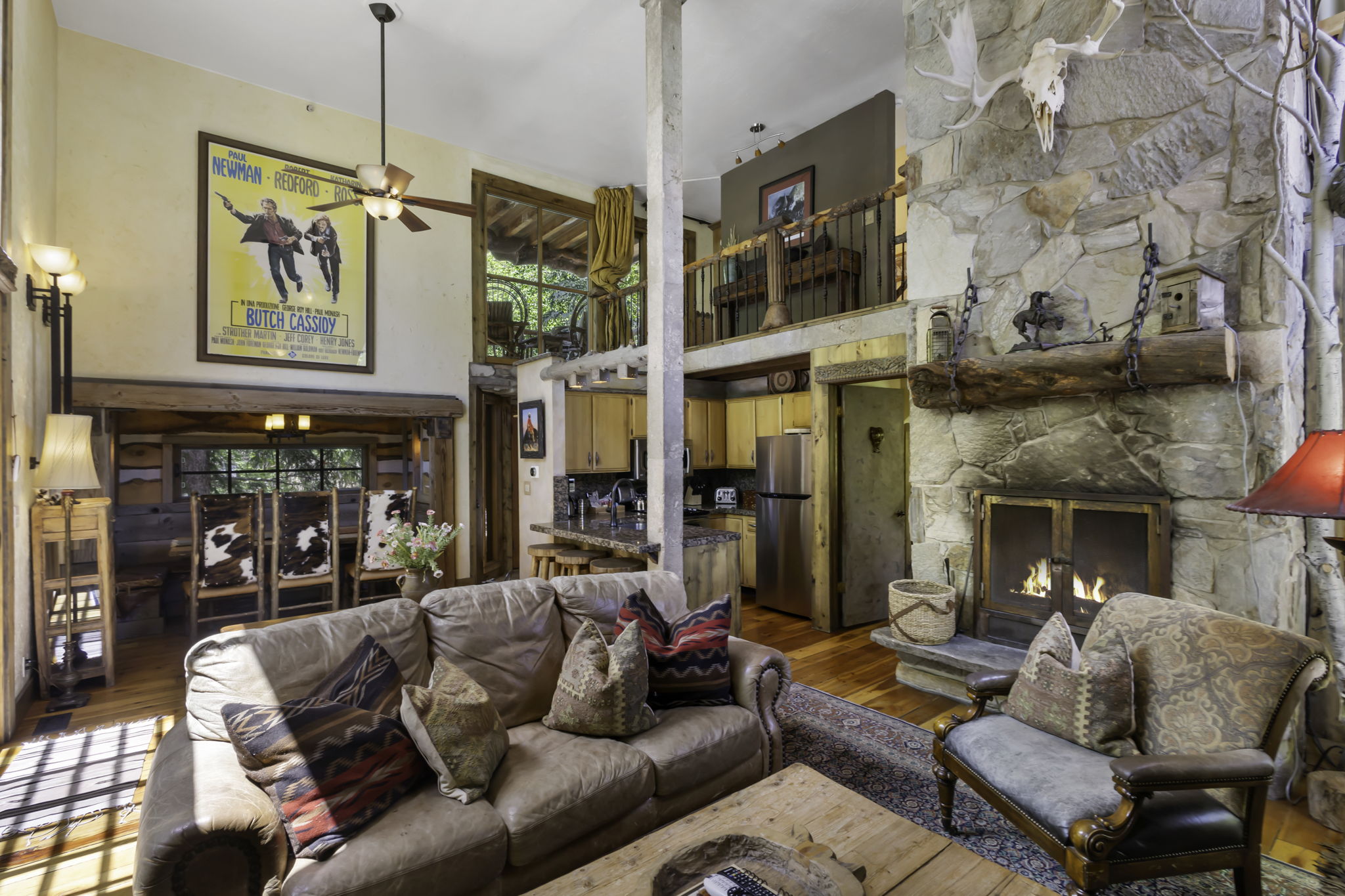 Open-concept living space featuring a floor-to-ceiling stone fireplace with a wood mantle, hardwood flooring, and a second-story balcony overlooking the room