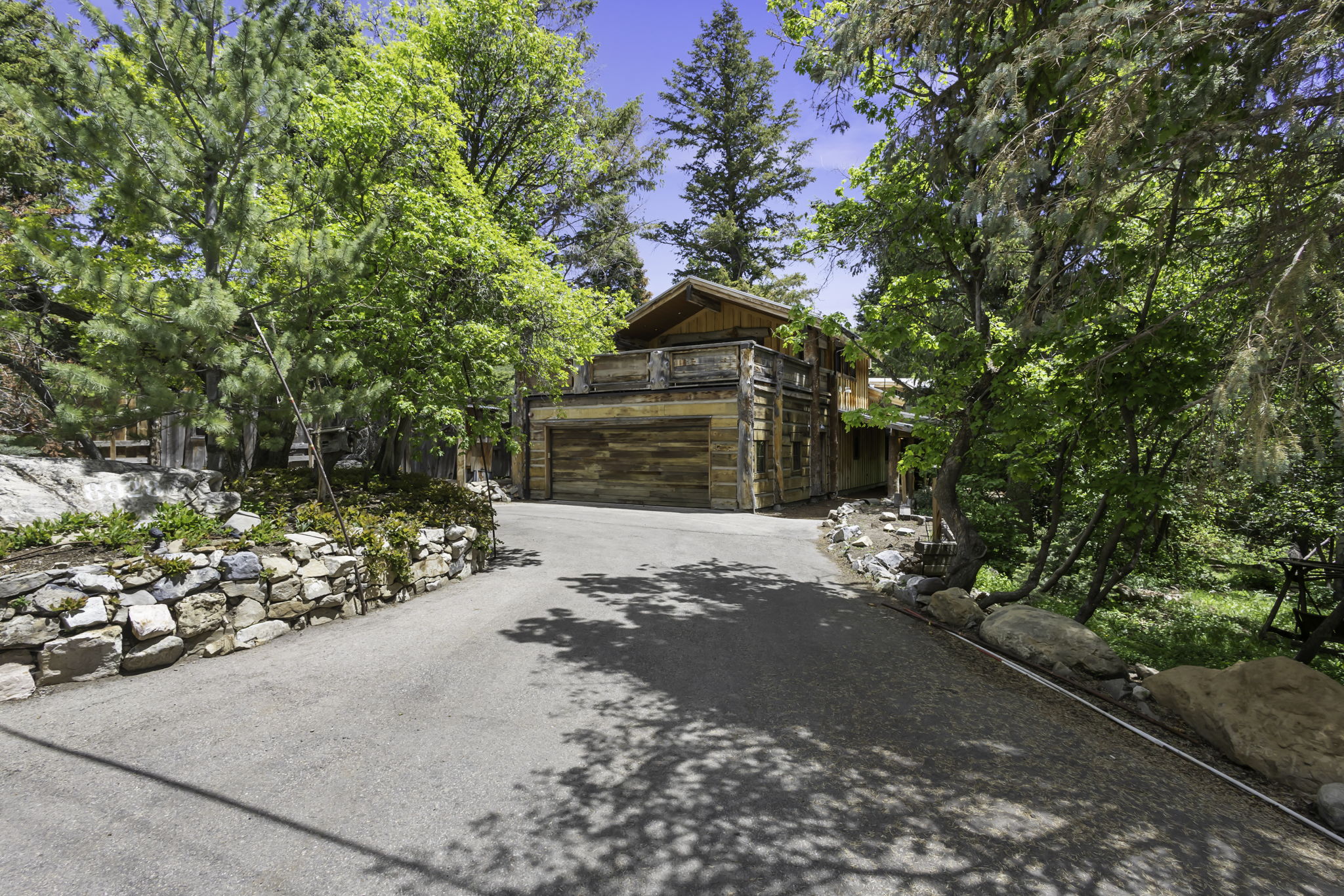 Asphalt driveway curving towards a multi-level wood-sided residence with an integrated garage