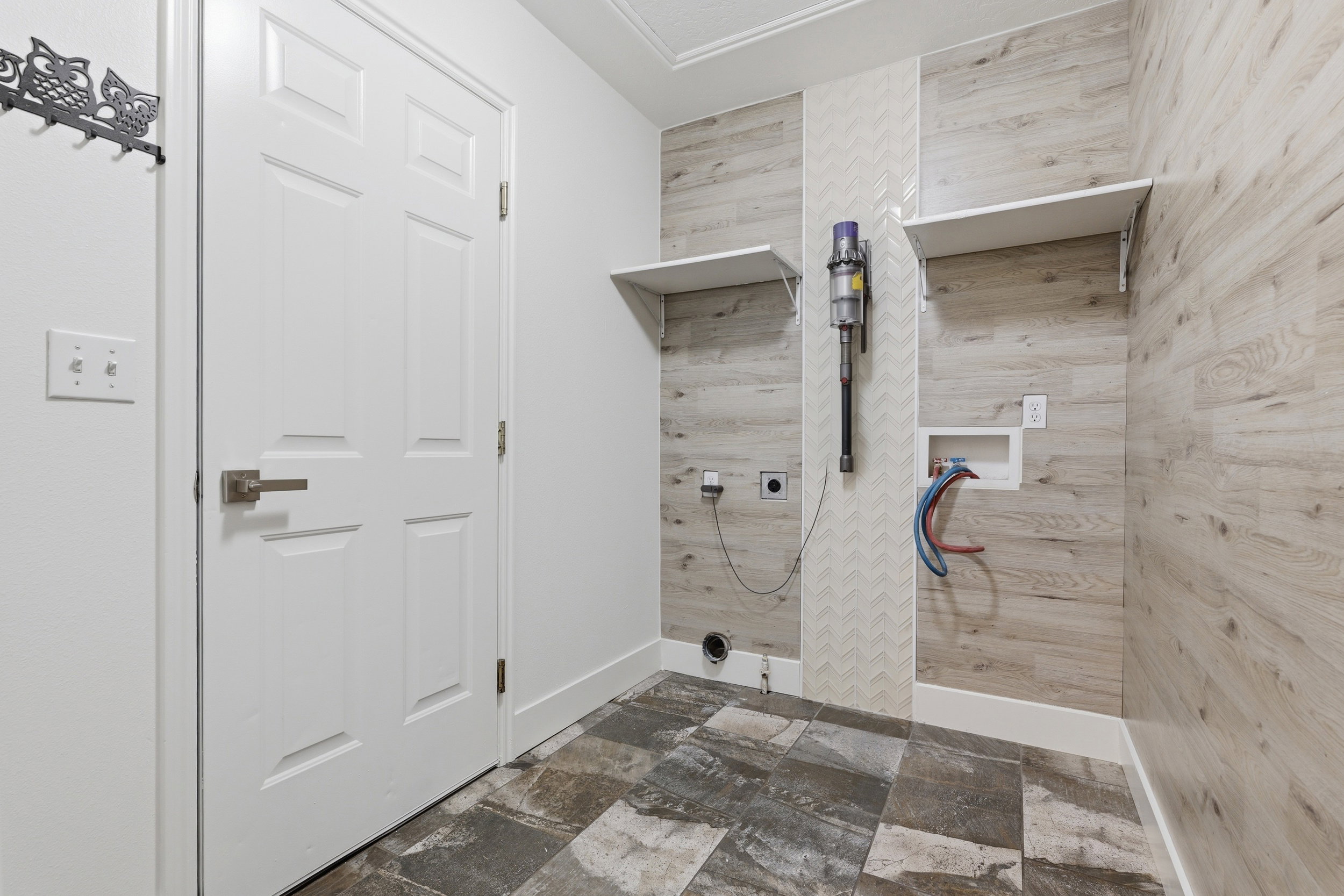 Utility space featuring wood-look wall paneling with a chevron accent, two built-in shelving units, and durable floor tiling