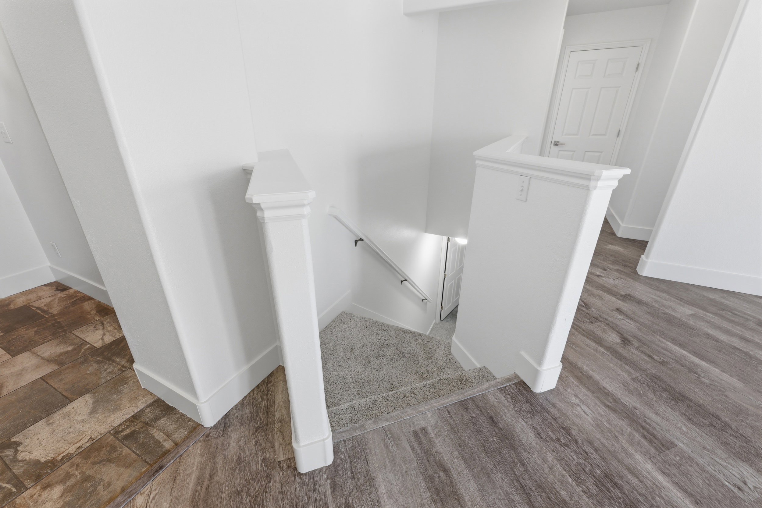 Carpeted staircase with white balusters, wood-finish flooring, and white baseboards