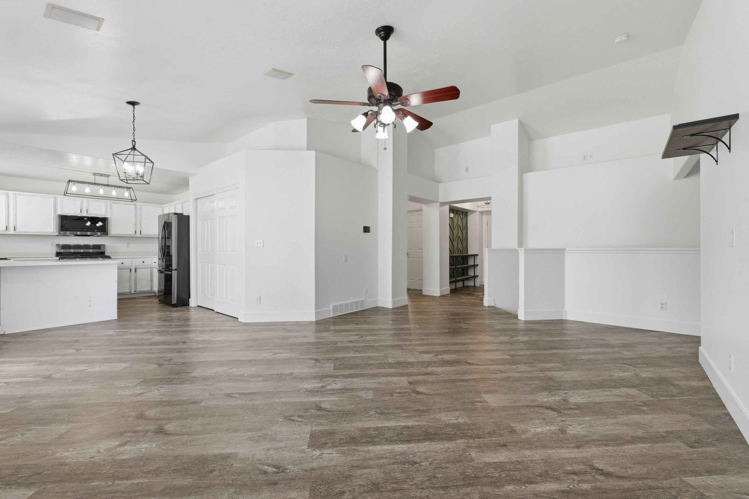 Open-concept living area with wood-finish flooring, vaulted ceilings, and a modern ceiling fan