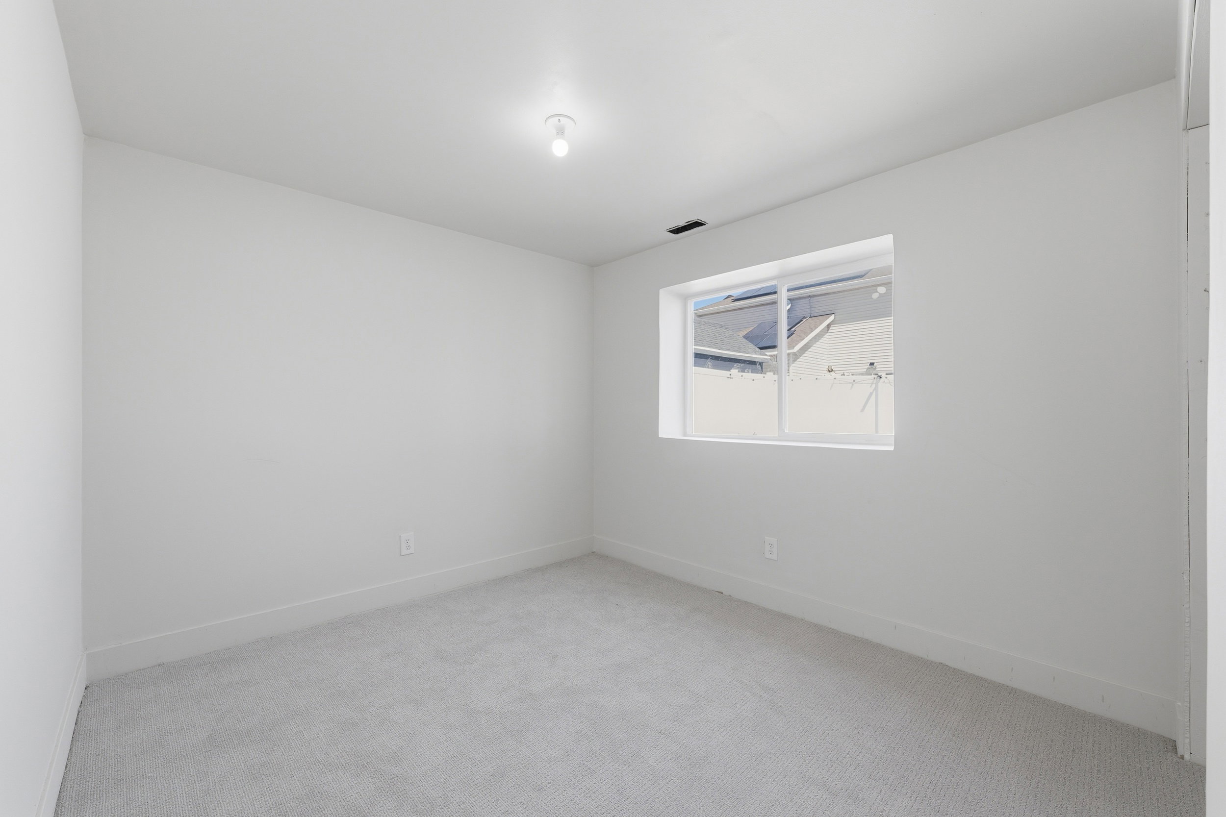 Carpeted interior room featuring a single-pane window, white walls, and a ceiling-mounted light fixture
