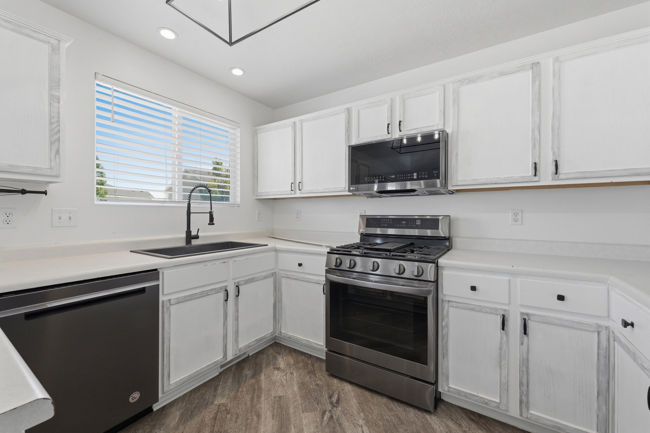 Kitchen featuring white cabinetry, light-toned countertops, a stainless steel gas range, built-in microwave, and wood-finish flooring