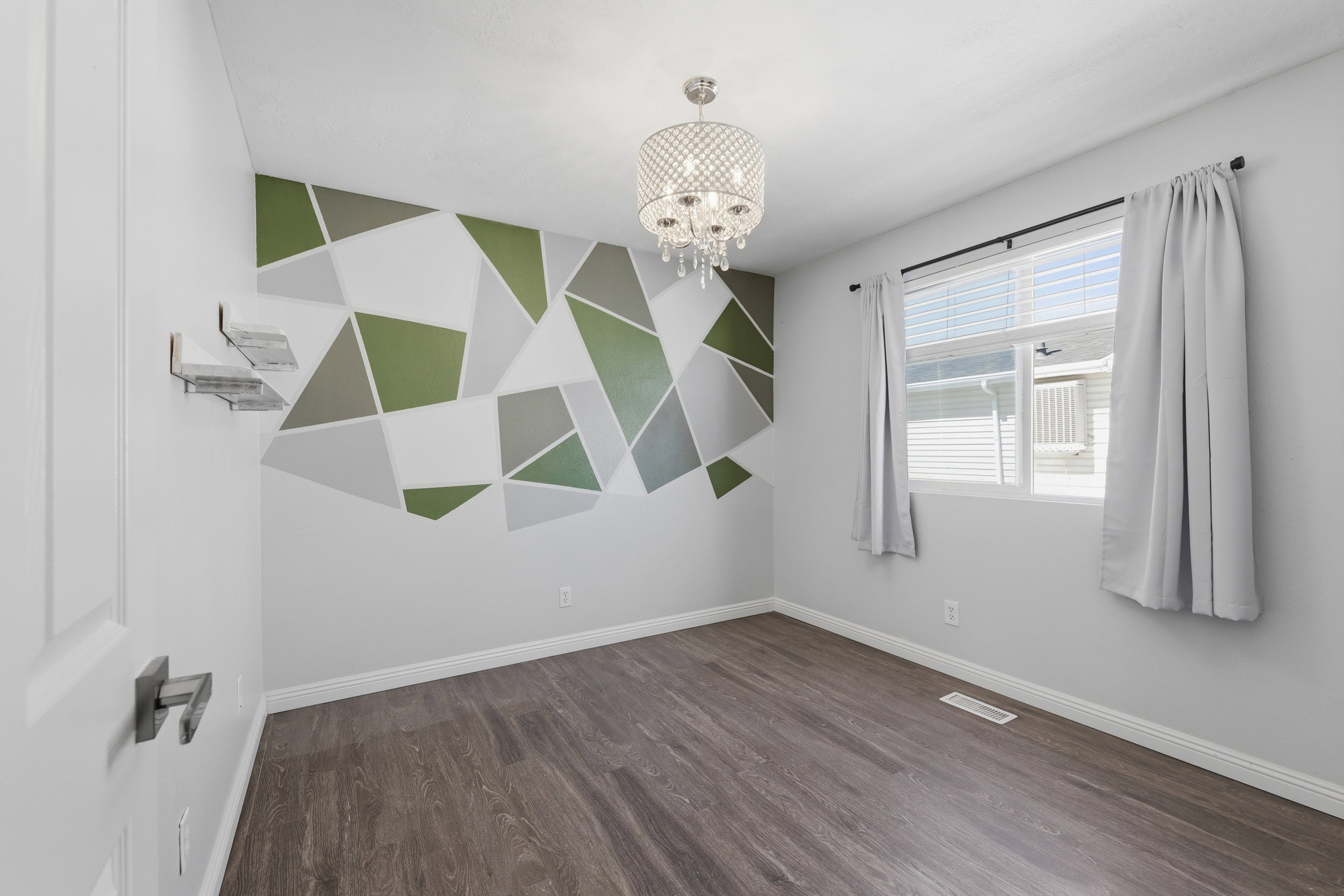 Interior room featuring wood-finish flooring, a decorative accent wall with geometric patterns, and a ceiling-mounted chandelier