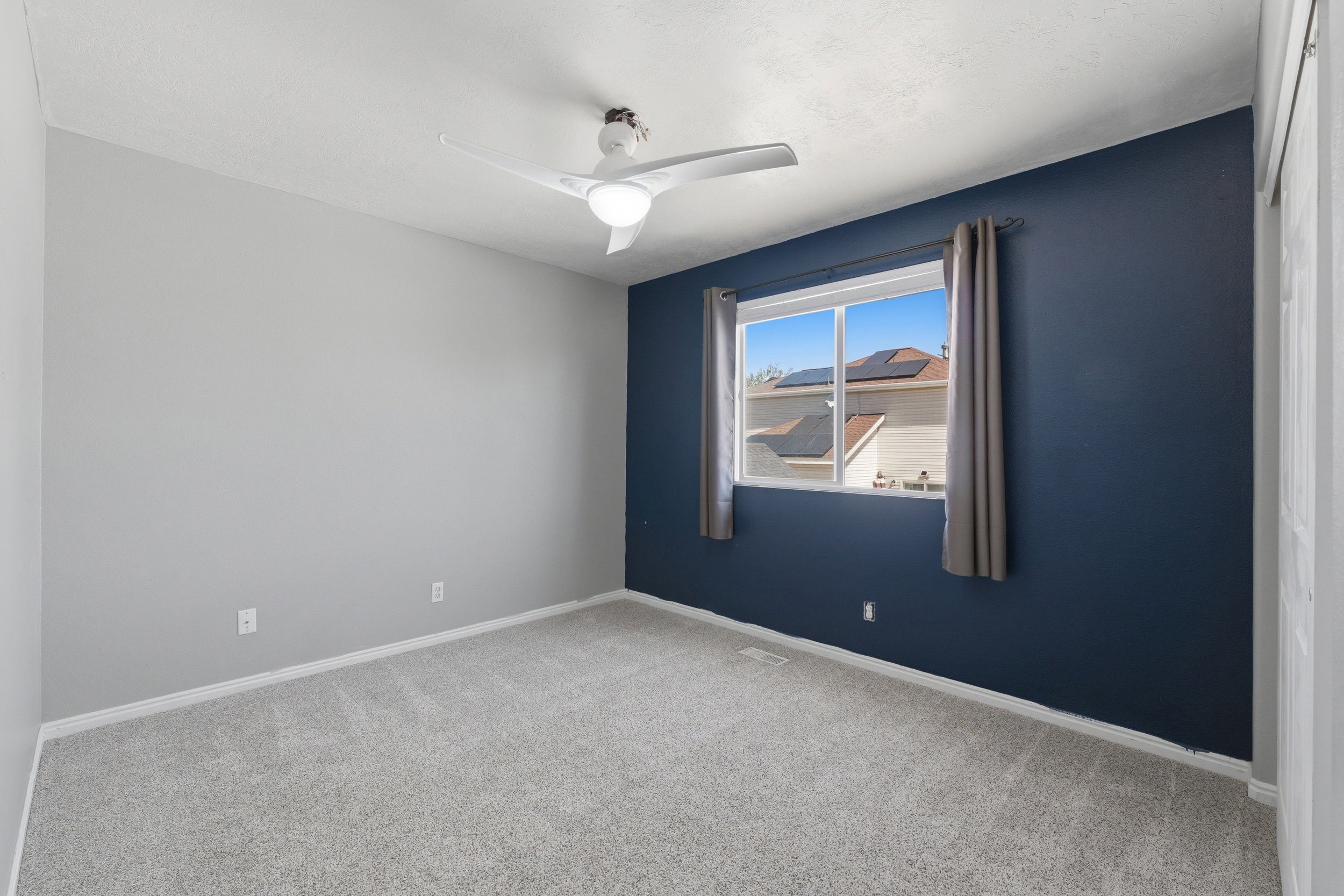 Bright room featuring soft gray walls with a bold accent wall, a window with natural light, a ceiling fan, and light-colored carpeting
