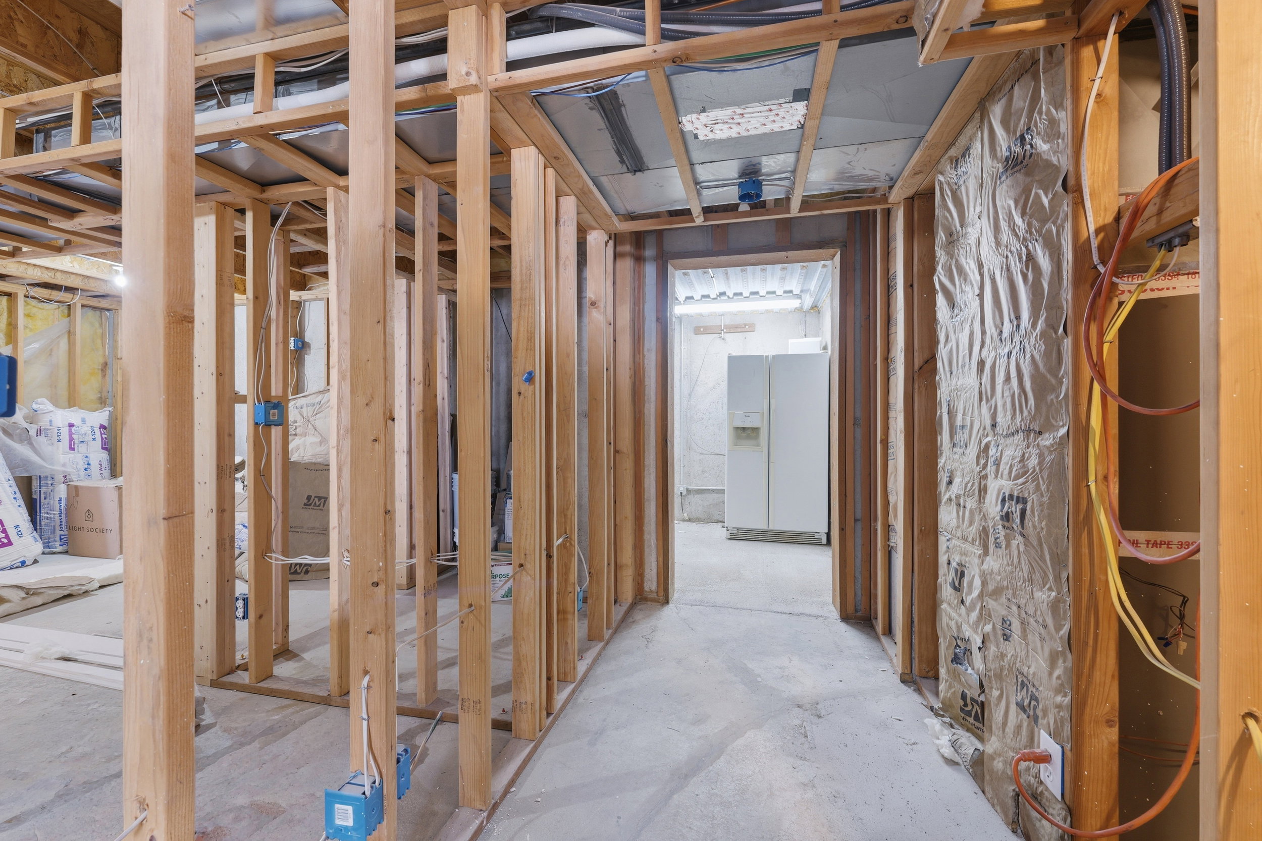 Unfinished basement space featuring exposed wooden framing, visible electrical wiring, and insulation