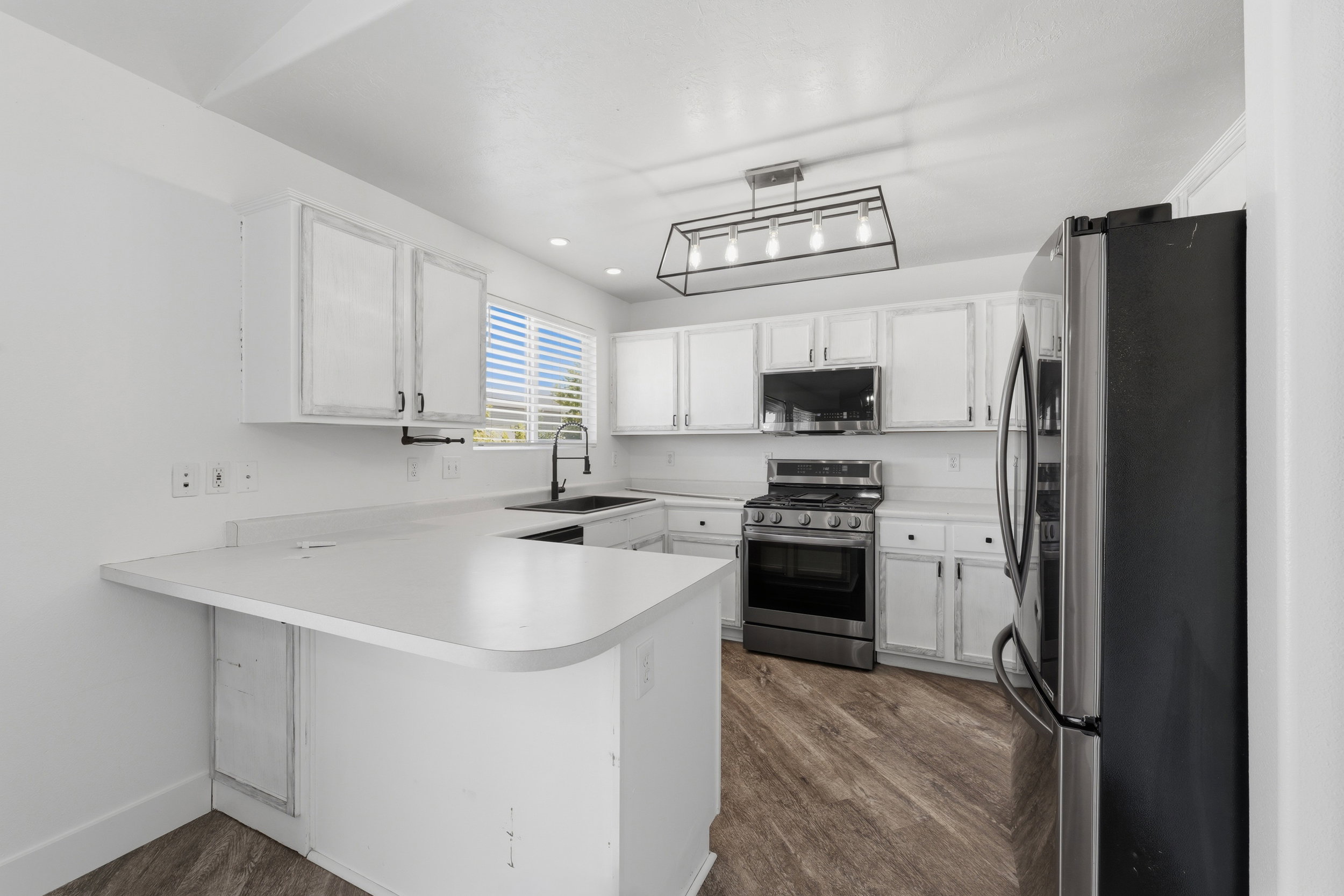 Kitchen featuring white cabinetry, light countertops, stainless steel appliances, wood-finish flooring, and a modern linear chandelier