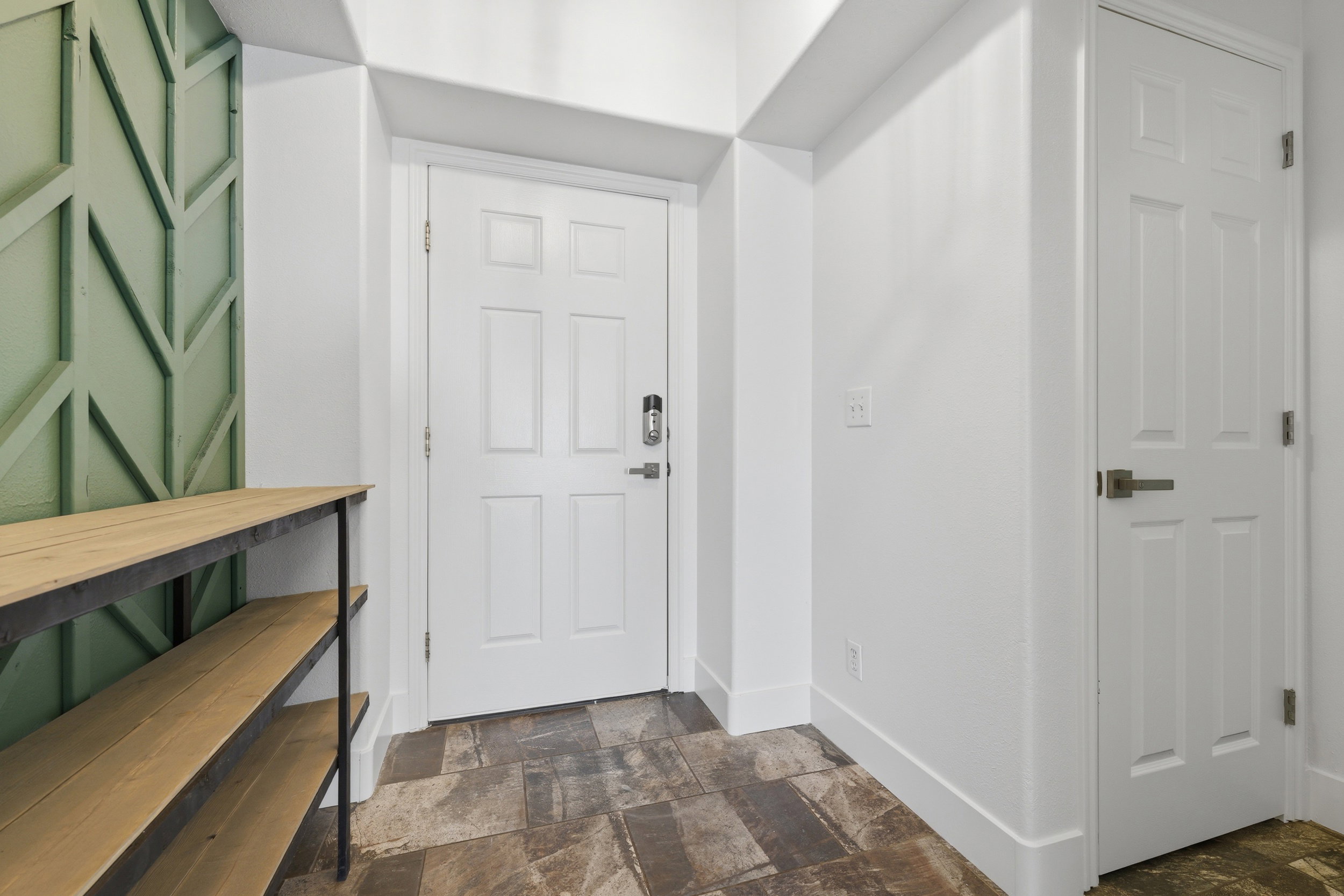 Entryway featuring patterned accent wall, tile flooring, white six-panel doors, and ample wall space