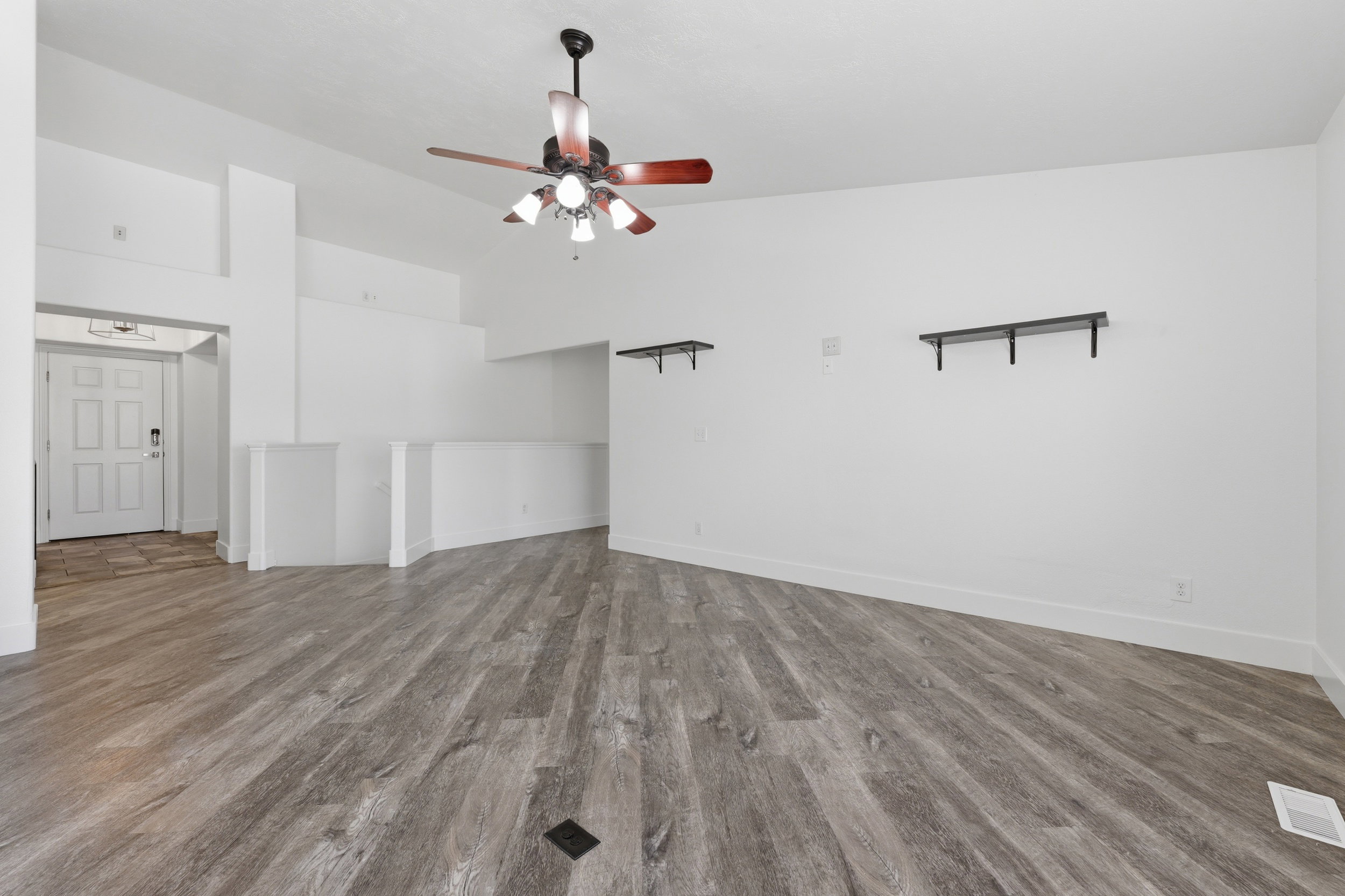 Spacious interior featuring wood-finish flooring, a modern ceiling fan with integrated lighting, and white walls