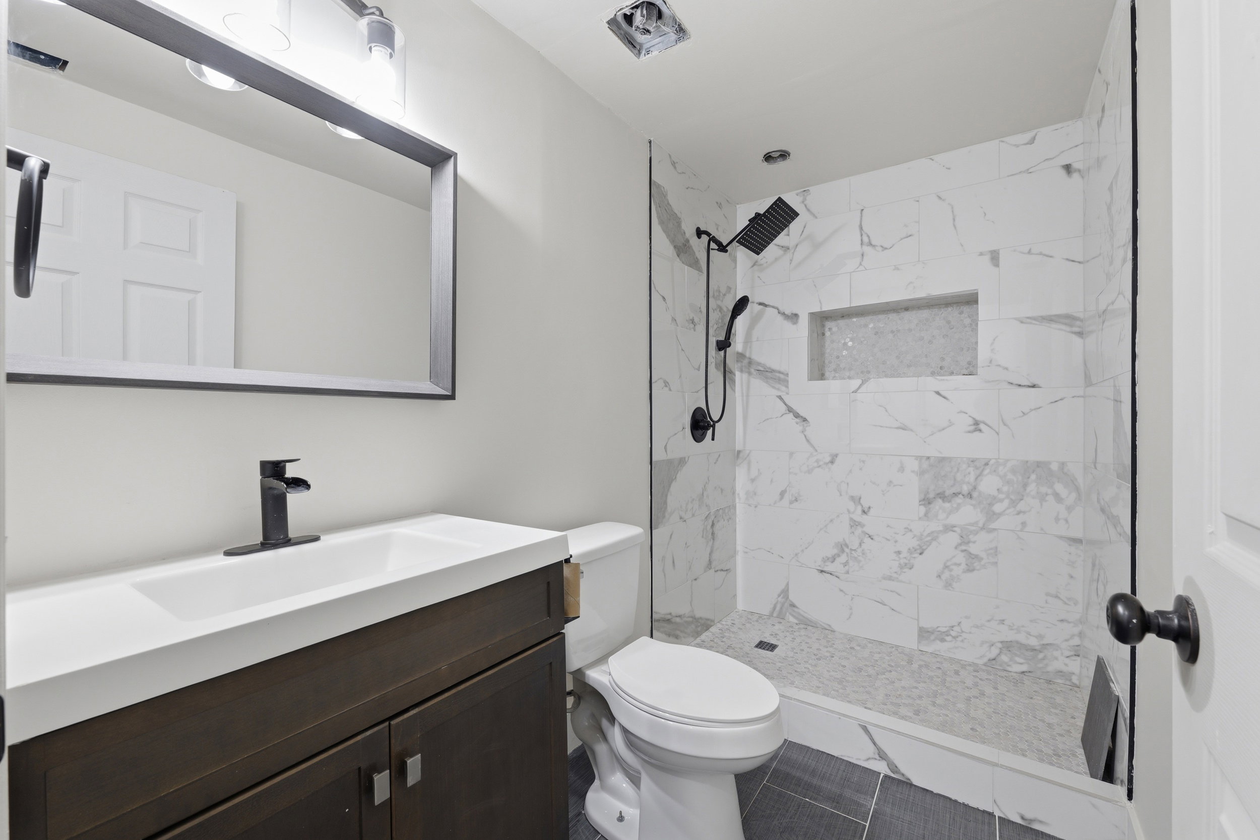 Modern bathroom featuring a walk-in shower with white and gray tiled walls, a built-in shower niche, and a contrasting dark gray mosaic tile floor