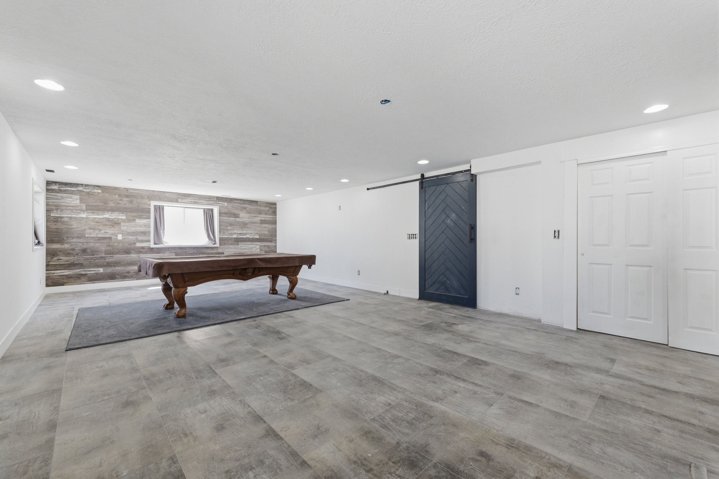 Spacious room featuring wide plank wood-finish flooring, recessed ceiling lighting, and a prominent accent wall with horizontal wood paneling