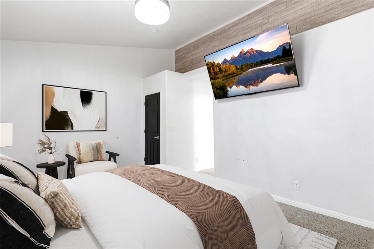 Carpeted bedroom with white walls, a mounted television, and wood-finish ceiling accents Virtually staged