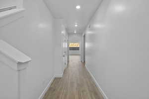Hallway featuring recessed lighting, wood-finish flooring, white baseboards, and a neutral wall palette