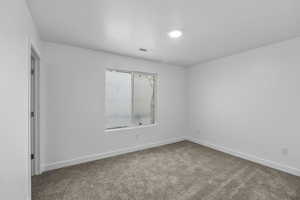 Neutral white walls with recessed ceiling lighting, a window with white trim, and plush carpeting