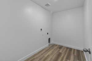 Laundry area featuring wood-finish flooring, white baseboards, light-colored walls, and a ceiling-mounted light fixture