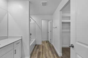 Bathroom featuring a white vanity with integrated sink, a full-size mirror, a shower-tub combination, and wood-finish flooring
