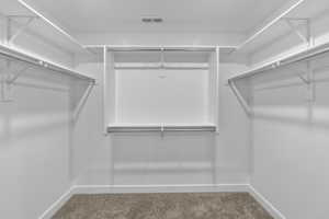 Walk-in closet with built-in shelving, multiple hanging rods, and neutral-toned carpeting