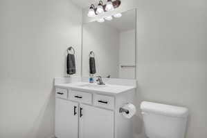 Bathroom vanity with a white countertop and integrated sink, under-cabinet storage with black hardware, and a toilet