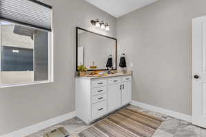 Bathroom vanity with a rectangular basin, light-toned countertop, and white cabinetry
