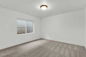 Neutral-toned room featuring a single window with a window well, light-colored walls, and a patterned carpet
