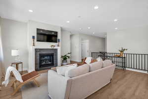 Living area featuring a floor-to-ceiling fireplace with dark gray brick surround and white mantel, wood-finish flooring, recessed lighting, and a black metal railing
