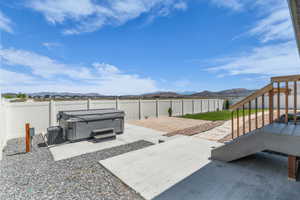 Fenced backyard featuring a built-in hot tub, concrete patio areas, a low-maintenance gravel ground cover, and a strip of green lawn