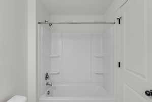 White fiberglass tub and shower combination featuring integrated shelving and a chrome shower fixture
