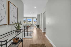 Hallway featuring light wood-finish flooring, recessed lighting, white baseboards, and neutral wall paint