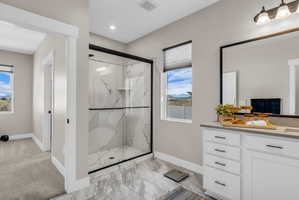 Spacious bathroom featuring a glass-enclosed shower with marble-look tile, a double vanity with ample storage, a large framed mirror, and a window providing natural light and mountain scenery