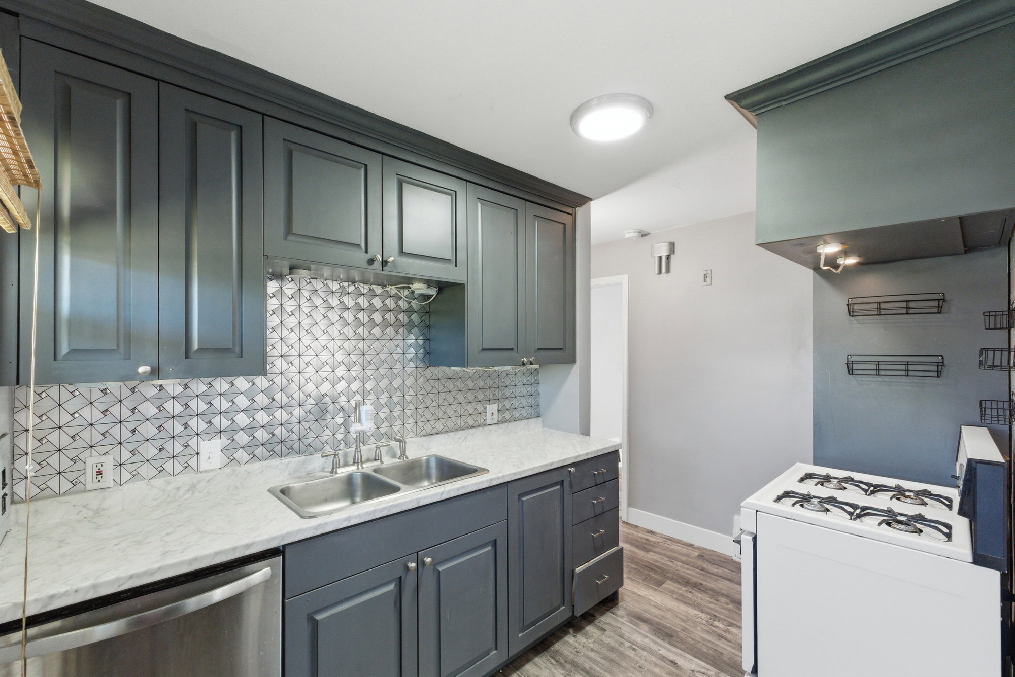 Updated kitchen featuring dark cabinetry, patterned tile backsplash, stainless dishwasher, and gas range.