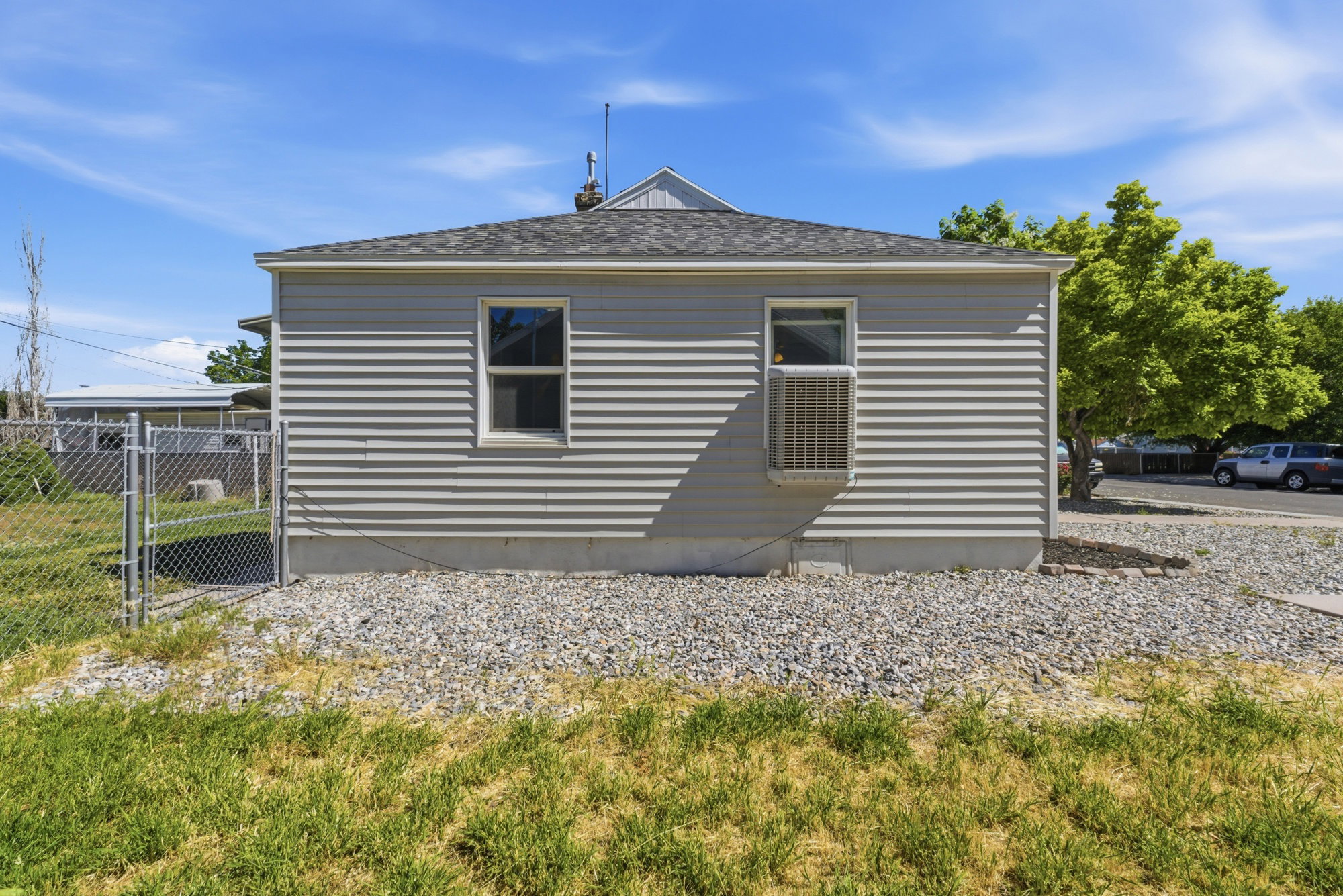 Side exterior view showing updated siding, rock landscaping, side yard access, and window A/C unit.