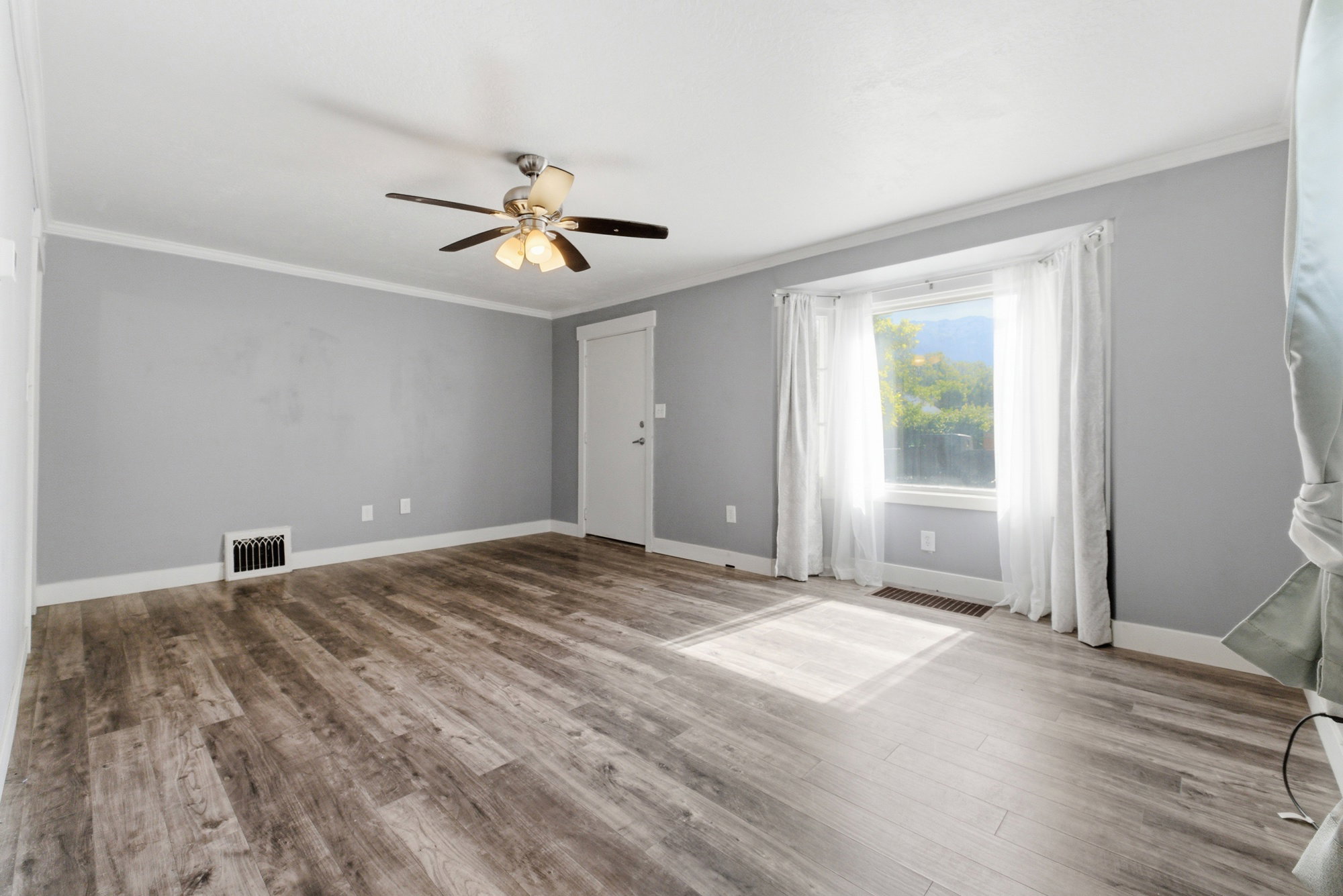 Additional view of the living room showing bright window, updated flooring, neutral finishes, and inviting natural light.