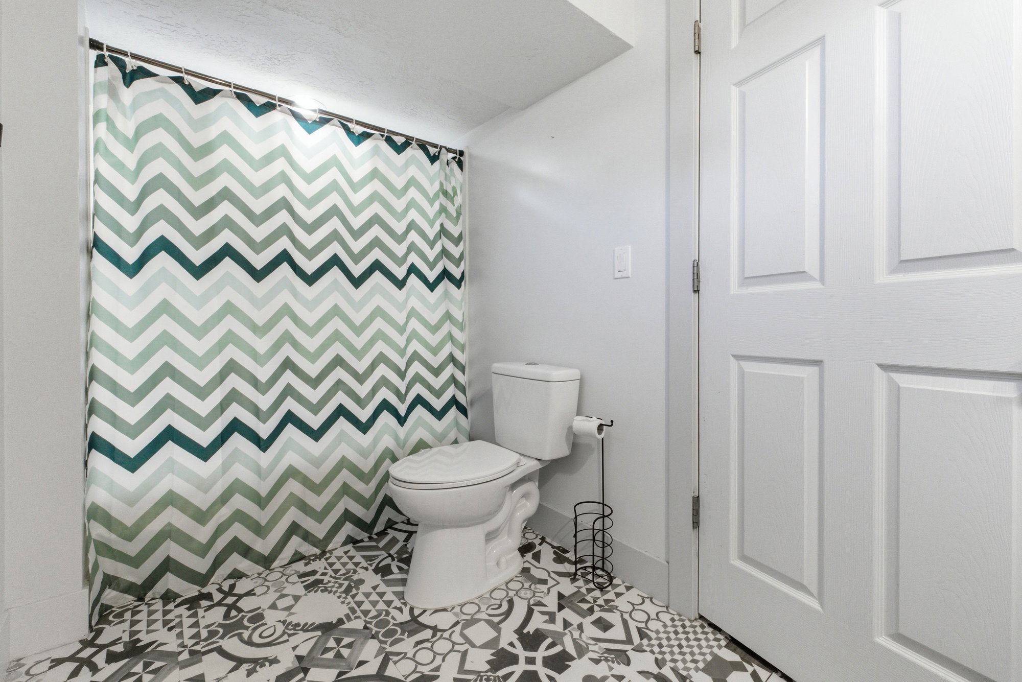 Bathroom with tub/shower combo, chevron shower curtain, patterned tile flooring, and bright neutral walls.