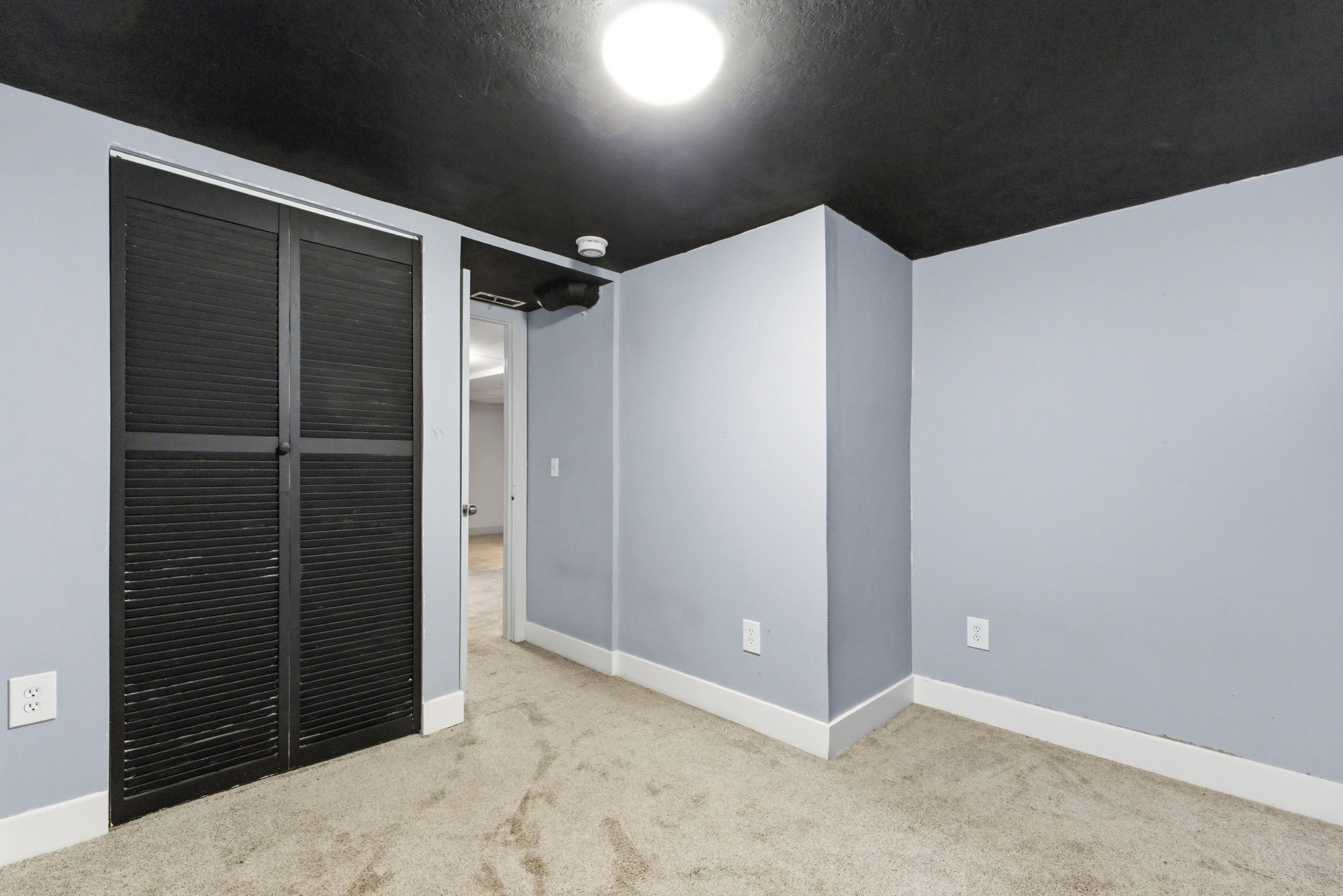 Flexible lower-level room with carpet, gray walls, black ceiling detail, closet, and neutral trim.